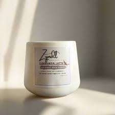 Cinnamon Latte coffee candle in a white hydrostone vessel bathed in natural sunlight. The label clearly shows it's a coconut wax candle with coffee candle scent featuring coffee, sugar, oat and cinnamon. This best coffee scented candle creates a cozy atmosphere with its 30-hour burn time, ideal for coffee and candles lovers.